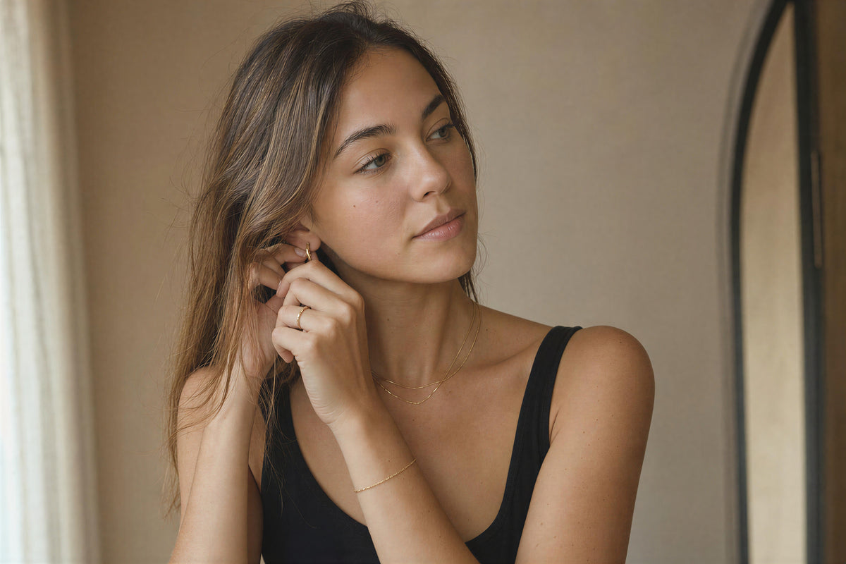Woman wearing layered Valesstra necklaces and hoop earrings with a white blouse in the city.