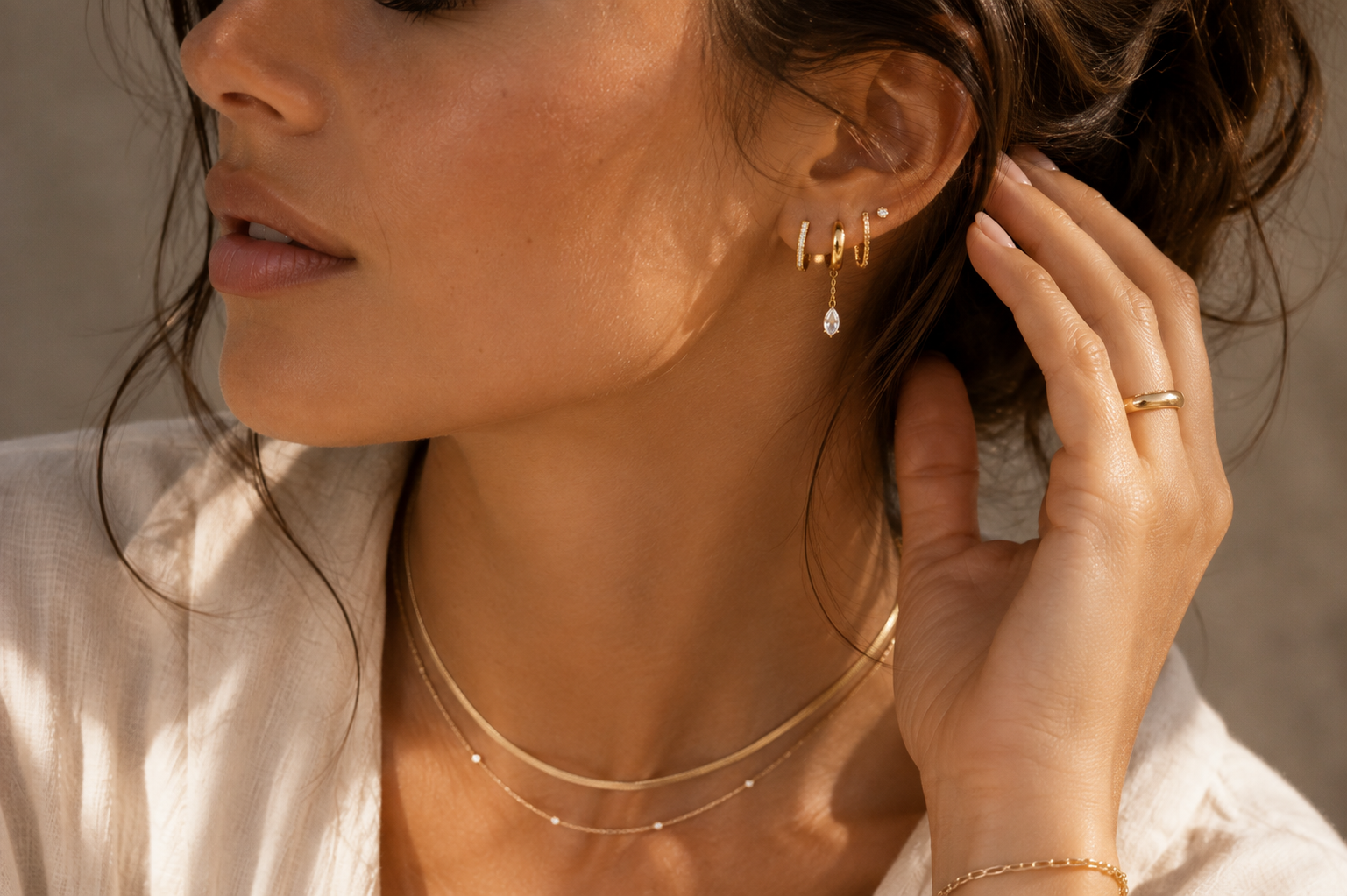 Woman wearing layered gold huggie and stud earrings in warm natural light.