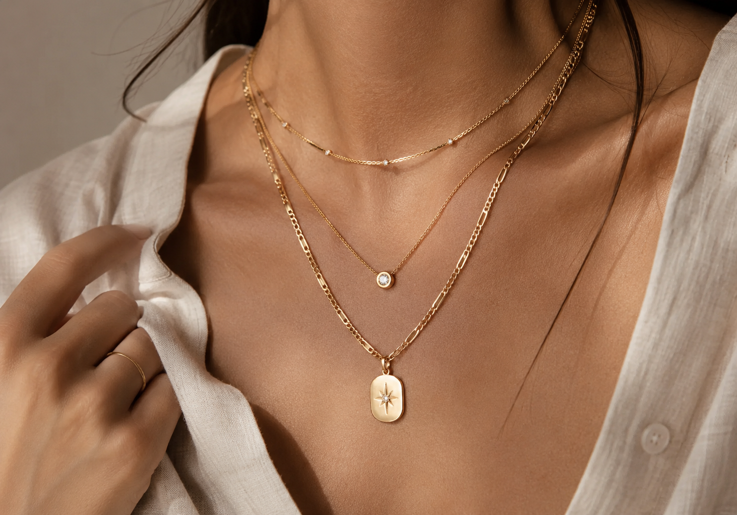 Layered gold necklaces styled over a white linen blouse in warm natural light.