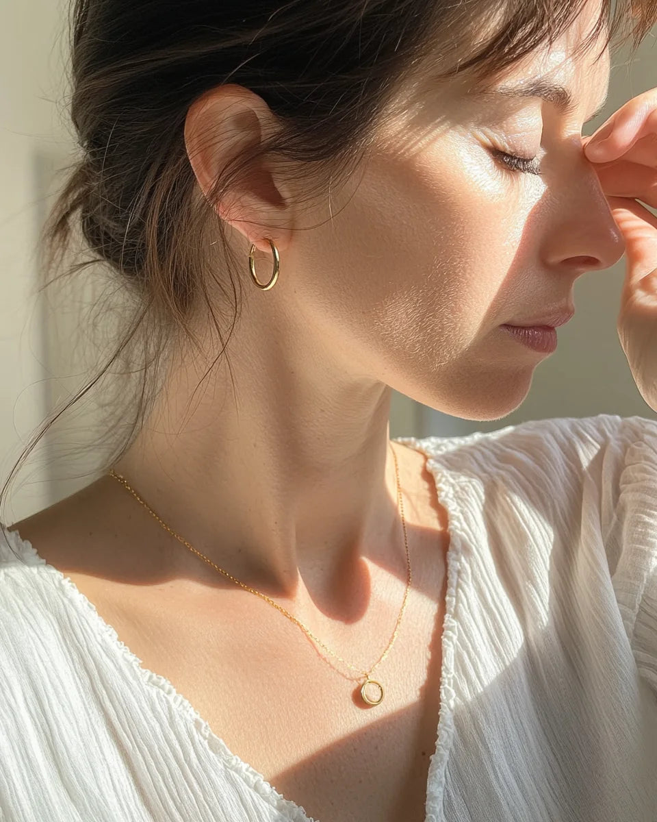 Woman wearing a delicate pendant necklace and gold hoop in natural light.