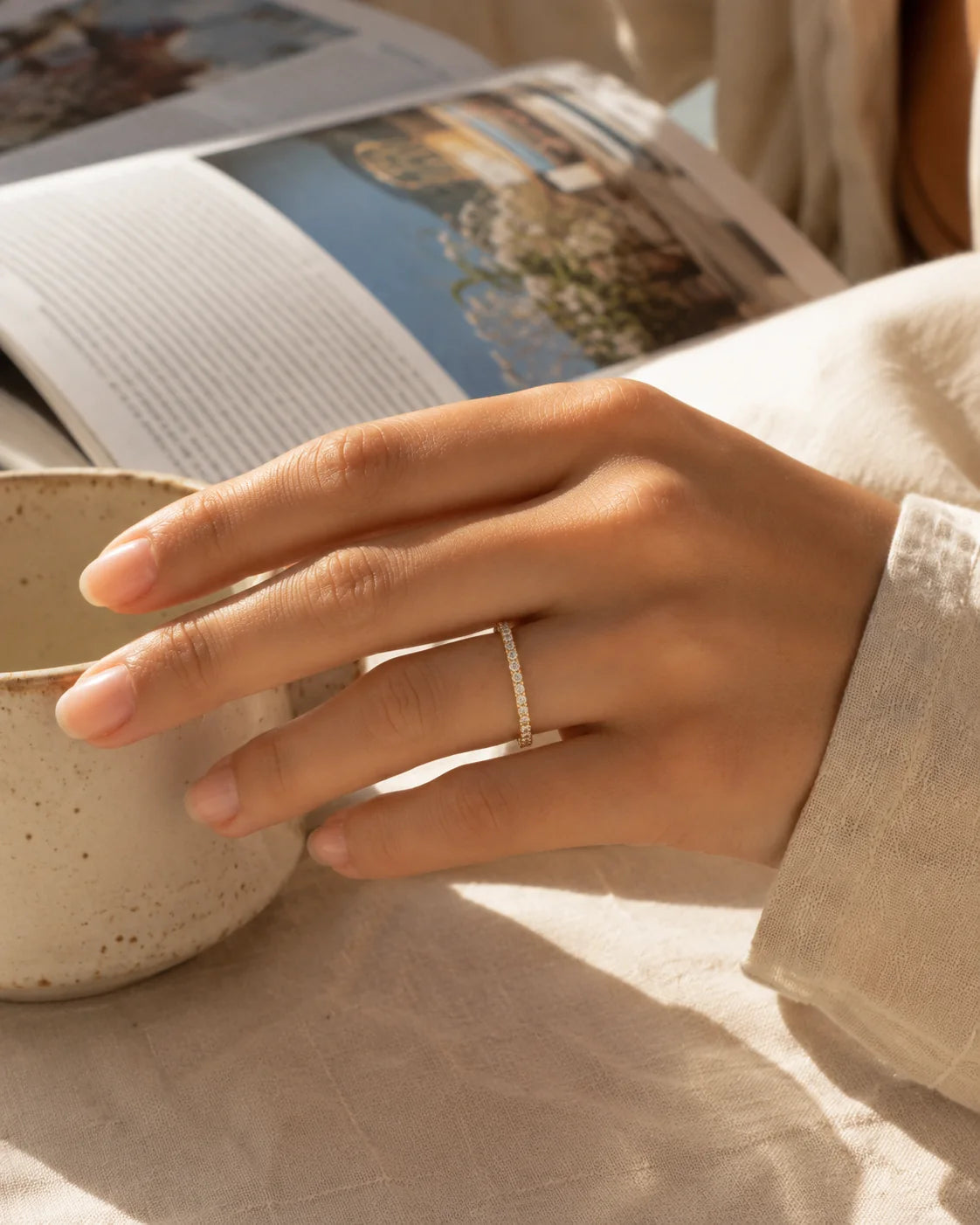 Hand wearing a delicate pavé ring beside a coffee cup.